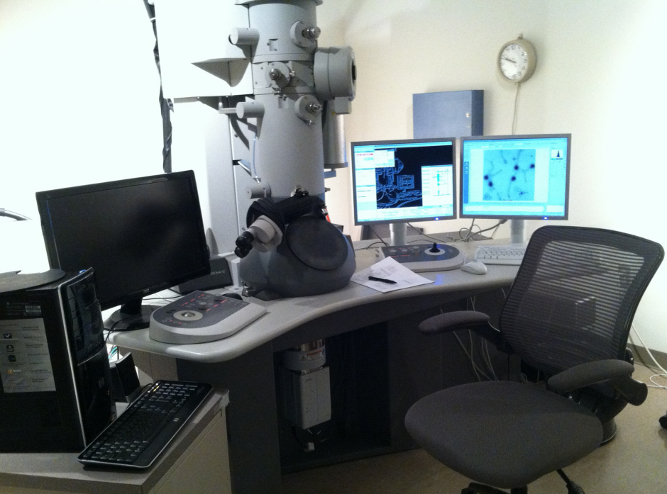 Una imagen de un escritorio con monitores de computadora y una microscopía electrónica de transmisión en la parte superior.